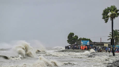 People gather along the sea shore amid rainfall in Kuakata on May 26, 2024, ahead of cyclone Remal's landfall in Bangladesh.