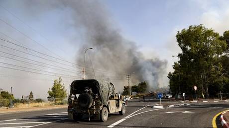 An Israeli military jeep is parked near a checkpoint as smoke rises from fires caused by rockets launched from southern Lebanon, in Upper Galilee, Israel, July 4, 2024