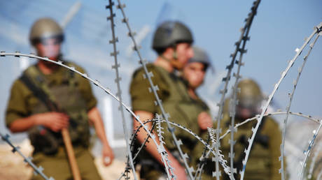 Four Israeli soldiers stand behind razor wire near the Palestinian village of Bil'in in the West Bank