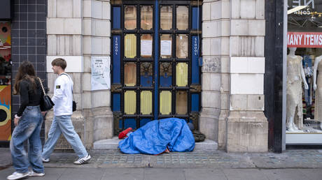 Homeless person sleeping in a doorway underneath a sleeping bag in London.