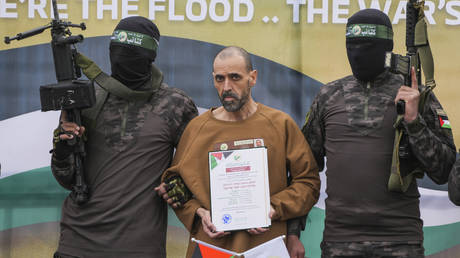 Israeli captive, Eli Sharabi, who has been held hostage by Hamas in Gaza since October 7, 2023, stands on a stage escorted by Hamas fighters before being handed over to the Red Cross in Deir al-Balah, central Gaza Strip, Saturday Feb. 8, 2025.