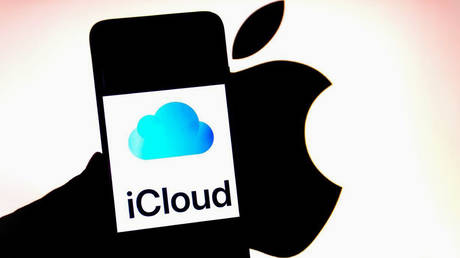  An iCloud logo is seen displayed on a smartphone with an Apple logo in the background.