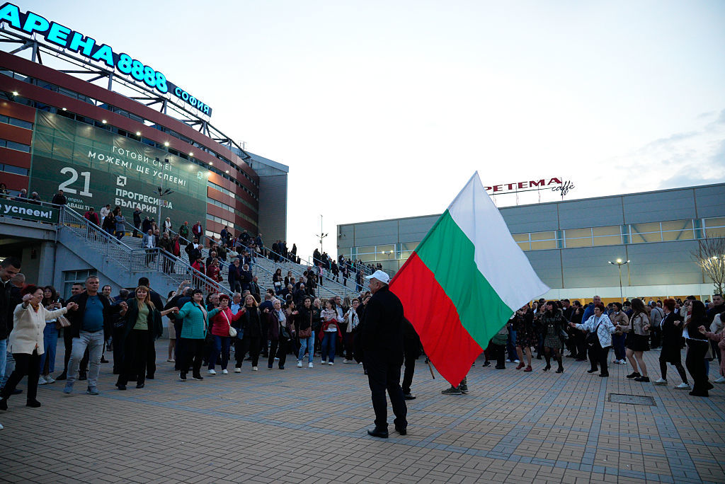 A man waves a Bulgarian flag while people perform a dance after a Progressive Bulgaria party rally in Sofia, Bulgaria, April 16, 2026
