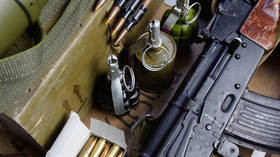A stock photo of an AK-47 assault rifle, rounds, and grenades in an army box.