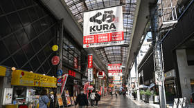 Pedestrians walk beneath a massive Kura Sushi advertisement in the Sennichimae shopping district of Osaka, Japan, April 3, 2026.