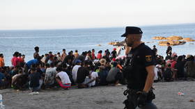 A police officer watches as migrants receive medical care from Red Cross volunteers  in Ceuta, Spain, August 7, 2026