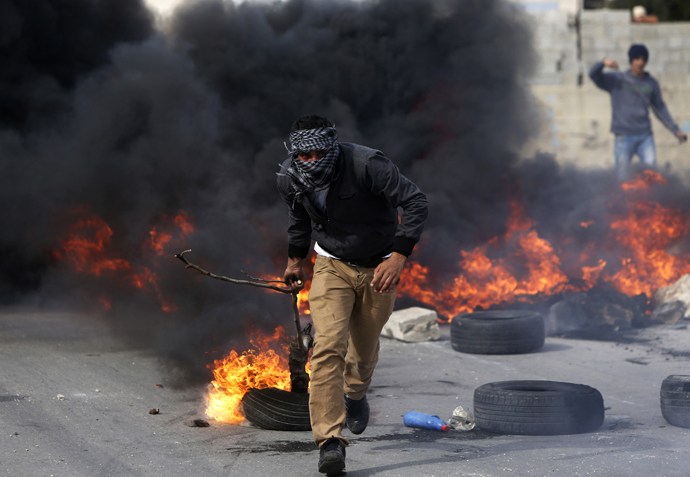 A stone-throwing Palestinian protester uses a branch to move a burning tyre during clashes with Israeli soldiers outside Israel's Ofer military prison near the West Bank city of Ramallah February 25, 2013. (Reuters / Mohamad Torokman)