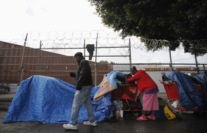Homeless people protect their possessions from the rain across the street from where the Skid Row Housing Trust's 102 pre-fabricated 350 square foot modular apartments are put in place downtown, becoming the first housing complex of its type for the homeless in the nation, in Los Angeles, California, December 18, 2012. (Reuters/Lucy Nicholson)