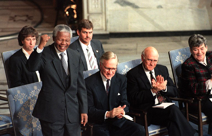 African National Congress President Nelson Mandela (L) salutes a South African choir while the president of the Nobel committee Dr. Francis Sejersted (C) and South African president Frederik De Klerk (R) applaud the choir's performance, 10 December 1993 in Oslo, where both leaders received the 1993 Nobel Peace Prize. (AFP Photo / Gerard Julien)