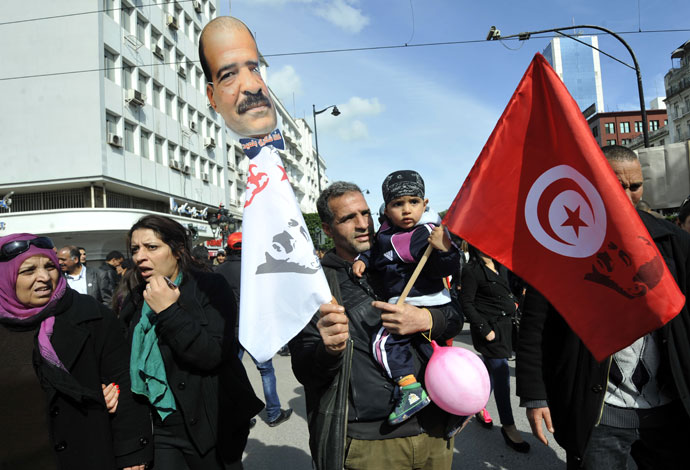 A Tunisian young boy holds a national flag in his father's arms during a demonstration to mark the 40th day of mourning after the death of anti-Islamist opposition leader Chokri Belaid (featured on poster) on March 16, 2013 .(AFP Photo / Fethi Belaid)