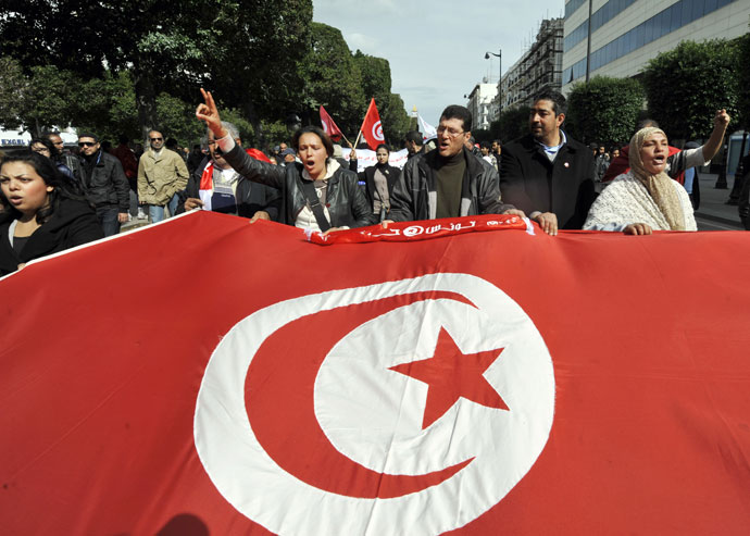Tunisian people wave a giant national flag during a demonstration to mark the 40th day of mourning after the death of anti-Islamist opposition leader Chokri Belaid (featured on poster) on March 16, 2013.(AFP Photo / Fethi Belaid)