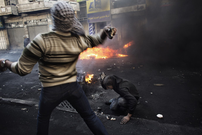 A Palestinian demonstrator throws stones towards Israeli security forces as his comrade breaks stones on the ground during clashes in the West Bank city of Hebron on April 4, 2013. (AFP Photo)
