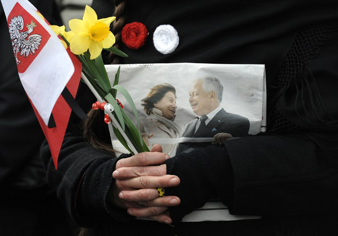 A person holds a Polish flag and a photo of late Polish presidential couple during a public memorial service on Pilsudski square in Warsaw on April 17, 2010. (AFP Photo / Joe Klamar)