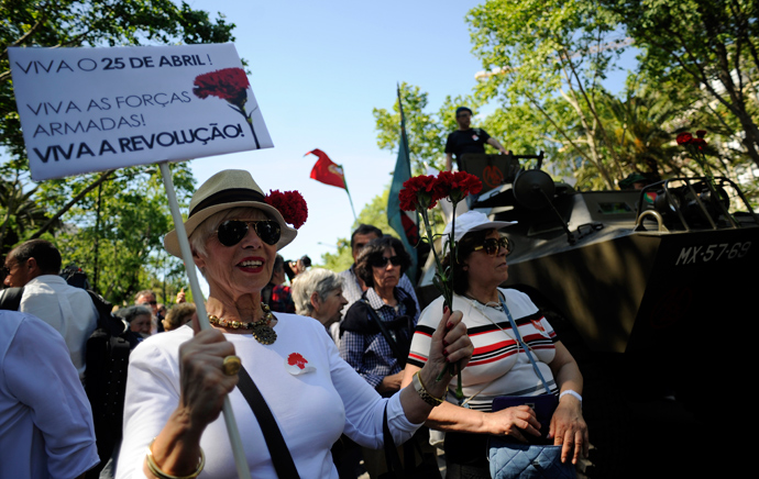 A woman holds red carnations and a board praising military forces and revoltion as she marches in Lisbon's main Liberdade Avenue during the celebration of the1974 Revolution anniversary on April 25, 2013 (AFP Photo / Francisco Leong)