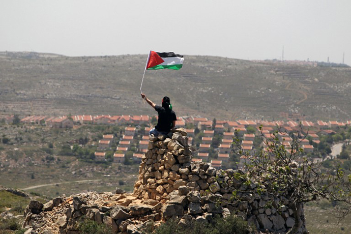 A Palestinian demonstrator from the West Bank village of Deir Jarir waves his national flag as he sits on a pile of rocks during clashes with Israeli soldiers on April 26, 2013. (AFP Photo / Abbas Momani)
