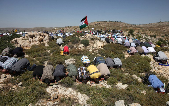 A Palestinian demonstrator from the West Bank village of Deir Jarir, waves his national flag as as others pray prior to clashes with Israeli soldiers on April 26, 2013. (AFP Photo / Abbas Momani)