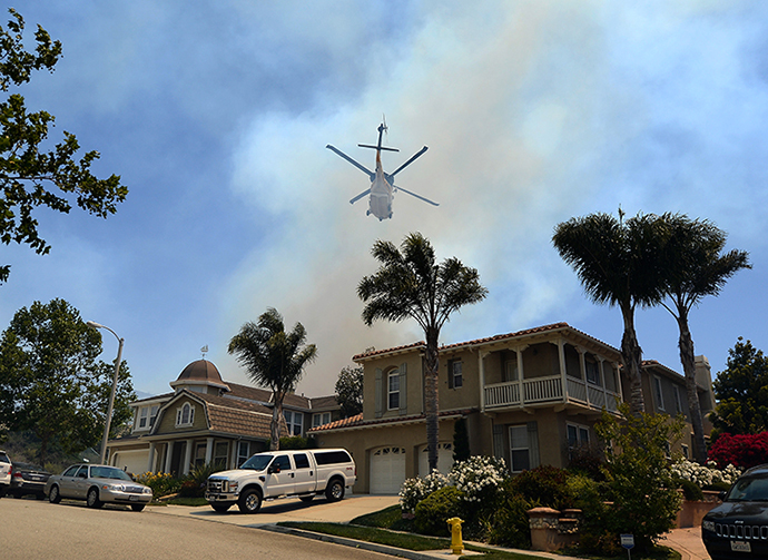 A fire fighting helicopter comes in to make a water drop behind some home threatened by a wildfire on May 2, 2013 in Newbury Park, California. (AFP Photo / Getty Images / Kevork Djansezian)