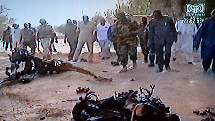 This video grab taken from Niger's TV public channel Tele Sahel on May 23, 2013 shows people standing in front of wreckage of the suicide bomber's motor vehicle, at the Agadez army base, northern Niger, following car bombings in Niger in which at least 20 people died (AFP Photo / Tele Sahel) 