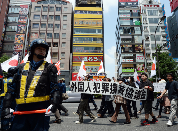 Riot police officers stand guard as demonstrators carrying Japanese flags march in a protest against crimes caused by foreign residents in Japan in the Shinjuku shopping district in Tokyo on May 26, 2013. Almost 100 rightists staged the protest march (AFP Photo / Toshifumi Kitamura)
