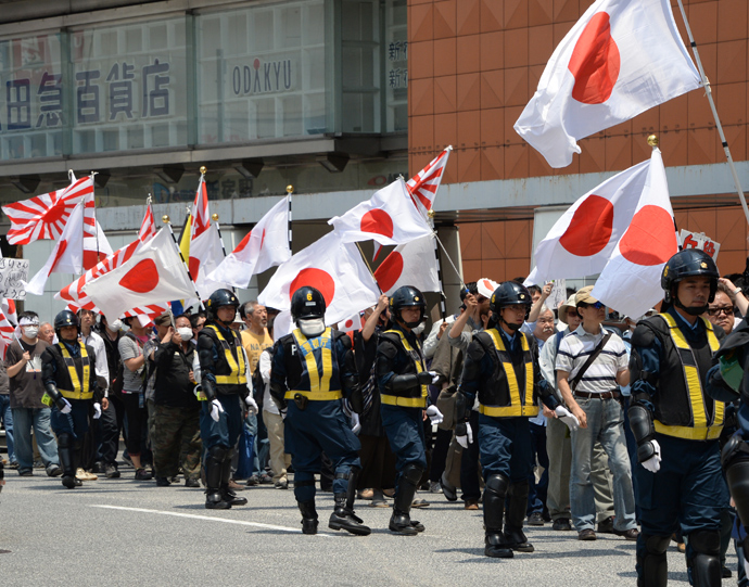 Protected by riot police officers, demonstrators carrying Japanese flags march in a protest against crimes caused by foreign residents in Japan at the Shinjuku shopping district in Tokyo on May 26, 2013 (AFP Photo / Toshifumi Kitamura)