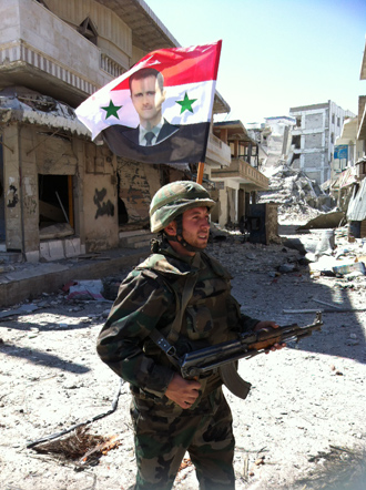 A Syrian army's soldier walks in a street left in ruins with a national flag featuring Syria's President Bachar al-Assad on June 5, 2013 in the city of Qusayr in Syria's central Homs province (AFP Photo / Str) 