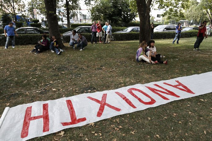 People sit behind a banner, which reads: "Open", outside Greek state television ERT headquarters after the government announced that it will shut down the broadcaster in Athens June 11, 2013. (Reuters / John Kolesidis)