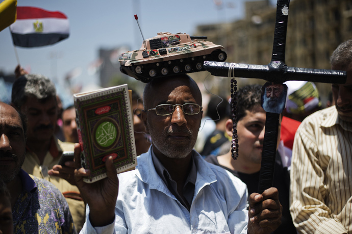 An Egyptian man, bearing a toy tank on his head, holds a cross (R) and a copy of the Koran, Islam's holy book, as people gather in Cairo's landmark Tahrir square after a night of celebrations following the toppling of ousted Egyptian president Mohamed Morsi on July 4, 2013 (AFP Photo / Gianluigi Guercia) 