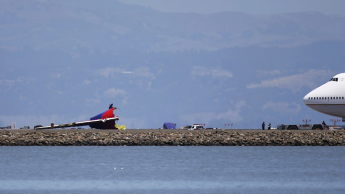 An airliner stands by as investihgators examine the wreckage of the tail section of an Asiana Airlines Boeing 777 which crash landied at San Francisco International Airport in San Francisco, California July 6, 2013. (Reuters/Stephen Lam)