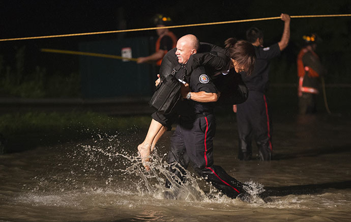A police officer rescues a woman from a Go Train, a commuter train, with passengers still waiting to be rescued inside, that is stuck in flood waters during a heavy rainstorm in Toronto, July 8, 2013. (Reuters / Mark Blinch)