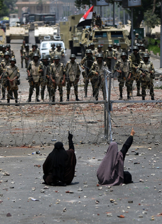 Two veiled Egyptian women, supporters of deposed president Mohamed Morsi, sit in front police standing behind barbed wire fencing that blocks the access to the headquarters of the Republican Guard in Cairo on July 8, 2013 (AFP Photo / Mahmud Hams) 