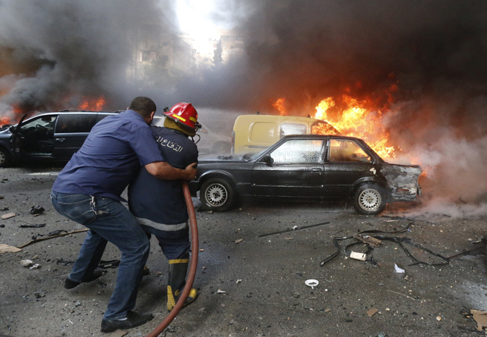 A firefighter is helped as he extinguishes fire at the site of an explosion in Beirut's southern suburb neighbourhood of Bir al-Abed on July 9, 2013 (AFP Photo / Str) 