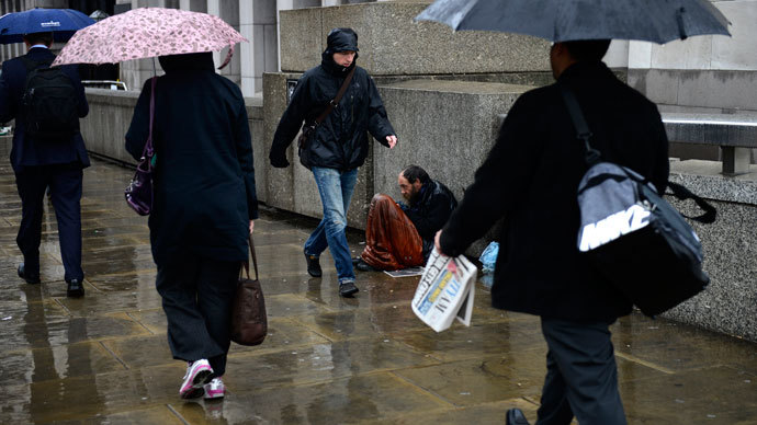 A homeless man sits in the rain as commuters make their way to work across London Bridge in London.(Reuters / Dylan Martinez)