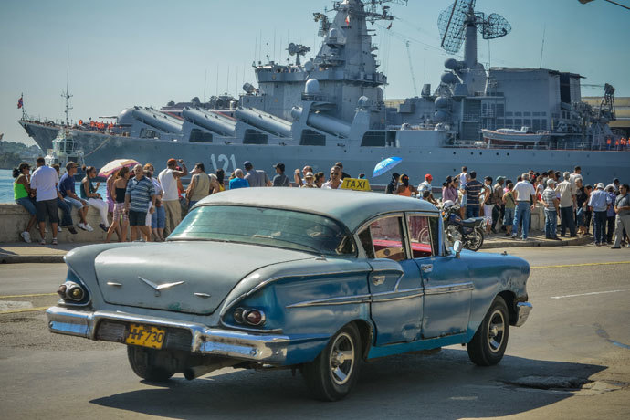 A vintage US-made car passes by as Cubans wave at the "Moskva" Russian guide missile cruiser arriving at Havana's harbour, on August 3, 2013.(AFP Photo / Adalberto Roque)