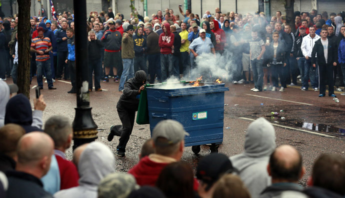 A loyalist protester pushes a garbage dumpster, that has been set alight, during clashes with the police as they wait for a republican parade to make its way through Belfast City Centre, August 9, 2013. (Reuters/Cathal McNaughton)