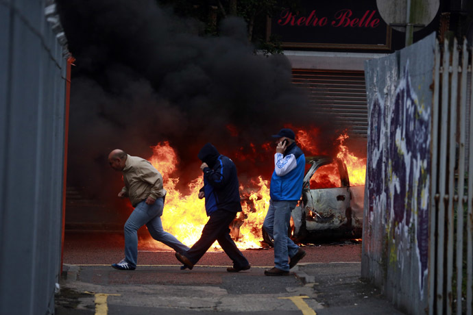 People run past a burning car after loyalist protesters attacked the police with bricks and bottles as they waited for a republican parade to make it's way through Belfast City Centre, August 9, 2013. (Reuters/Cathal McNaughton)