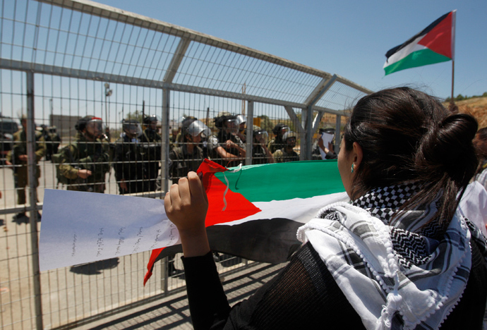 A Palestinian protester holds a flag in front of Israeli soldiers and border police during a protest outside Ofer prison near the West Bank city of Ramallah (Reuters / Mohamad Torokman)
