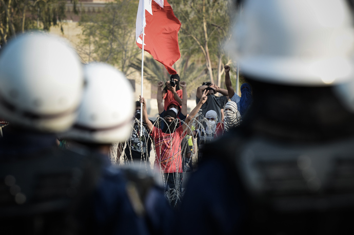 Riot police look on as Bahraini protestors shout anti-regime slogans and wave the national flag as they stand behind barbed wire placed by riot police during demonstration against the ruling regime in the village of Shakhora, west of Manama, on August 14, 2013 (AFP Photo / Mohammed Al-Shaikh) 