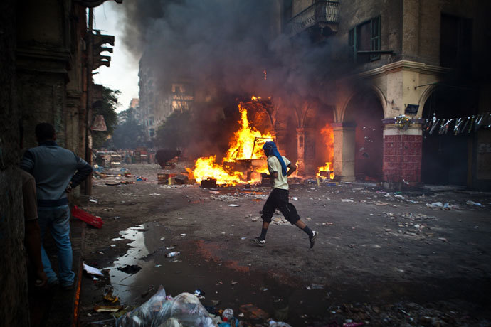 A supporter of the Muslim Brotherhood and of ousted president Mohamed Morsi runs past a burning vehicle during clashes with security officers close to Cairo's Ramses Square, on August 16, 2013.(AFP Photo / Virgnie Nguyen Hoang)