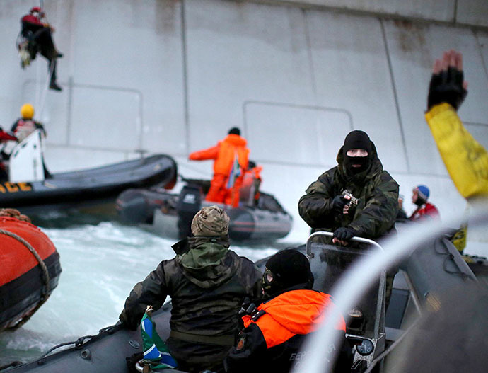 A handout photo taken by Greenpeace on September 18, 2013, shows a camouflage clad mask wearing officer of Russian Coast Guard (2nd R) pointing a gun at a Greenpeace International activist (partly seen R) during an environmentalists' attempt to climb Gazprom's 'Prirazlomnaya' Arctic oil platform somewhere off Russia north-eastern coast in the Pechora Sea. (AFP Photo / Greenpeace / Denis Sinyakov)