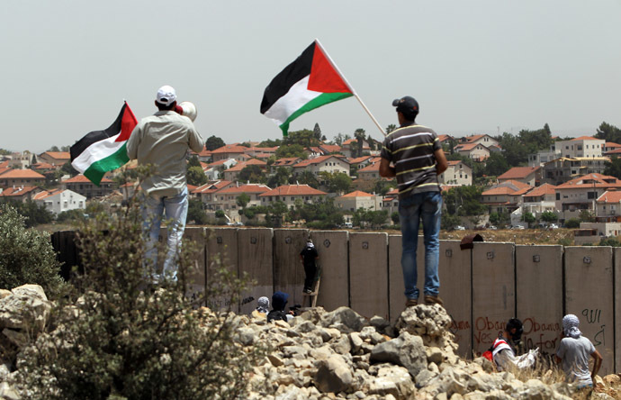 Palestinian protesters wave the national flag as their comrades climb Israel's controversial separation barrier during clashes with Israeli security forces following a demonstration against Israeli settlements and its separation wall, in the West Bank village of Nilin near the Jewish settlement of Hashmonaim (background), on May 31, 2013. (AFP Photo)
