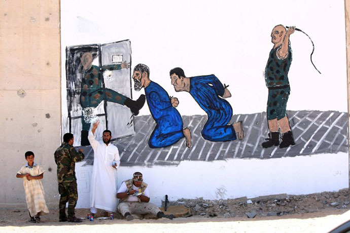 Libyans are pictured in front of a mural painting depicting a torture scene outside Tripoli's Abu Slim jail, scene of a 1996 massacre of prisoners, during a three-day exhibition in the gutted grey complex on June 29, 2012. (AFP Photo / Mahmud Turkia)