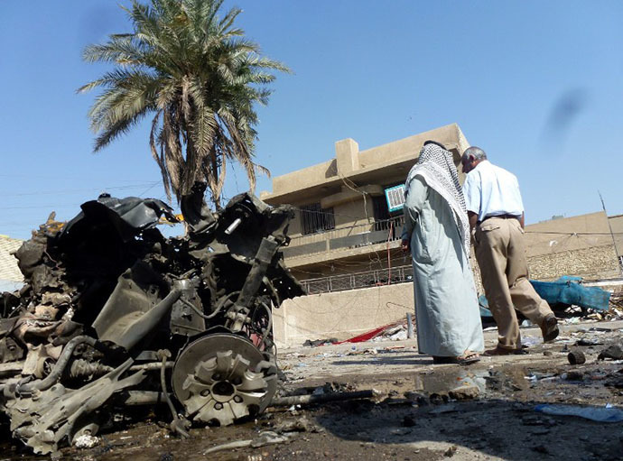 Iraqis look at the remains of a vehicle following an explosion at a small bus station on October 27, 2013, in the the Mashtal district of the capital Baghdad (AFP Photo / Sabah Arar)