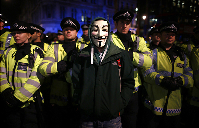A protester wearing a Guy Fawkes mask stands in front of a line of riot police officers during a protest against budget cuts and energy prices in Westminster, central London, November 5, 2013. (Reuters / Andrew Winning)