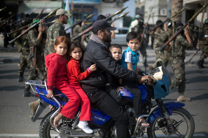 A Palestinian man rides a motorcycle with his children past masked militants of Ezzedine al-Qassam Brigades, Hamas's armed wing, as they parade in Jabalia refugee camp, northern Gaza Strip, on November 14, 2013 (AFP Photo / Mohammed Abed) 