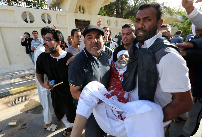 People assist a man who was injured after Libyan militiamen opened fire on a crowd wanting them to move out of their headquarters on November 15, 2013 in southern Tripoli. (AFP Photo / Mahmud Turkia)