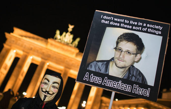 A supporter of the Anonymous group wearing a Guy Fawkes mask holds up a placard featuring a photo of US intelligence leaker Edward Snowden and reads "A true American Hero!" during a rally in front of Berlin's landmark Brandenburg Gate on November 5, 2013.(AFP Photo / Florian Scuhu)