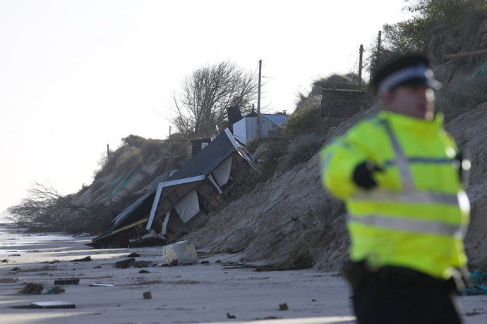 Emergency services personnel stand on the beach near a chalet home that was drawn into th sea during a tidal surge at Hemsby, in the east of England, on December 6, 2013. (AFP Photo / Justin Tallis) 