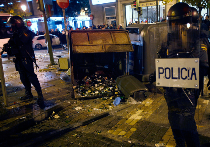 Spanish National Police officers in full riot gear stand near a trash container with broken glass bottles during clashes with protesters at the end of a protest against a new security law in Madrid December 14, 2013. (Reuters / Sergio Perez)