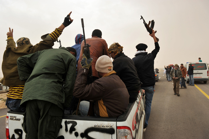 Libyan rebel fighters raise their weapons as they ride at the back of a pick-up truck on their way to battle against pro-Gaddafi forces, some 40 km down the road of the northcentral city of Ras Lanuf on March 4, 2011 (AFP Photo)