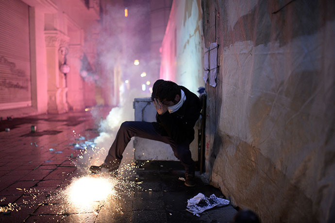 A protestor protects himself as fireworks explode on the Istiklal Avenue on December 27, 2013, during clashes between the Turkish police and protestors. (AFP Photo / Bulent Kilic)